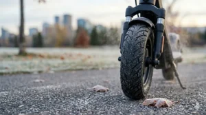 Close-up illustration of deep-tread pneumatic tires on an affordable cold weather electric scooter navigating wet, slushy Canadian city streets safely.
