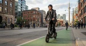 A commuter riding an electric scooter with removable battery along a downtown urban bike lane.