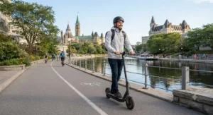 A relaxed commuter riding a mid-speed electric scooter for commuting beside the scenic Rideau Canal path in Ottawa.