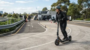 A reviewer testing a speed limited vs unrestricted electric scooter on a paved testing track outdoors.